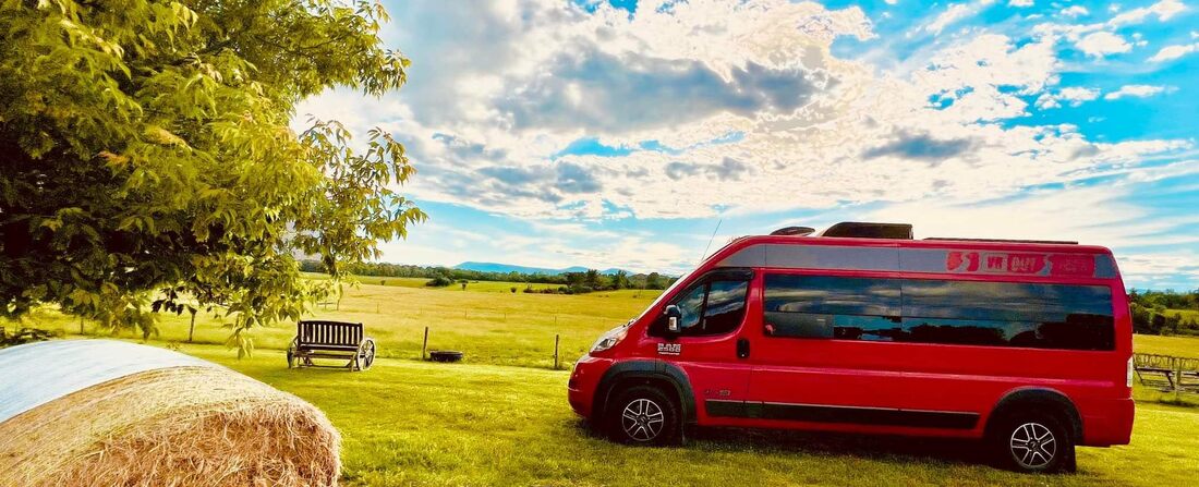 A red RV is parked next to a green pasture on a working farm that offers glamping in Vermont.