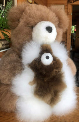 A large brown and white alpaca plush in the shape of a teddy bear poses with a smaller version of itself at this Vermont alpaca store.