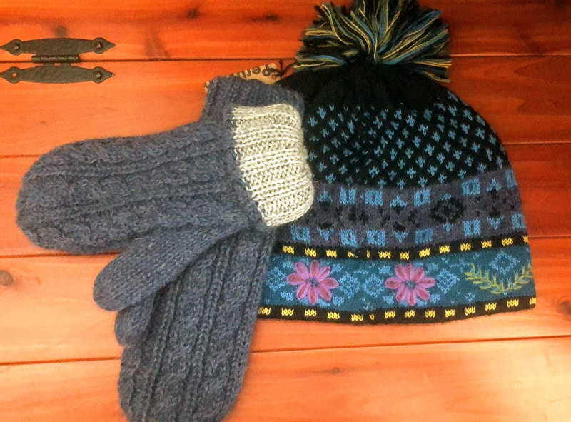 Gray alpaca mittens with a white inside are placed on top of a black and gray alpaca hat that has pink flowers on it.